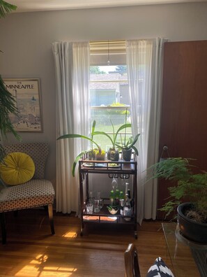 A room with a patterned sofa, a small table with drinks and glasses, a potted plant, and a poster on the wall. - Summer cozy & stylish 1 BR bath office for solo traveler in shared home. (Robbinsdale)
