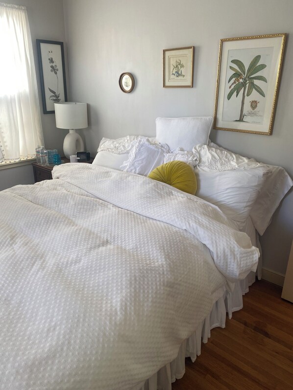 A neatly made bed with white linens, a bedside lamp, and a framed botanical print on the wall. - Summer cozy & stylish 1 BR bath office for solo traveler in shared home. (Robbinsdale)