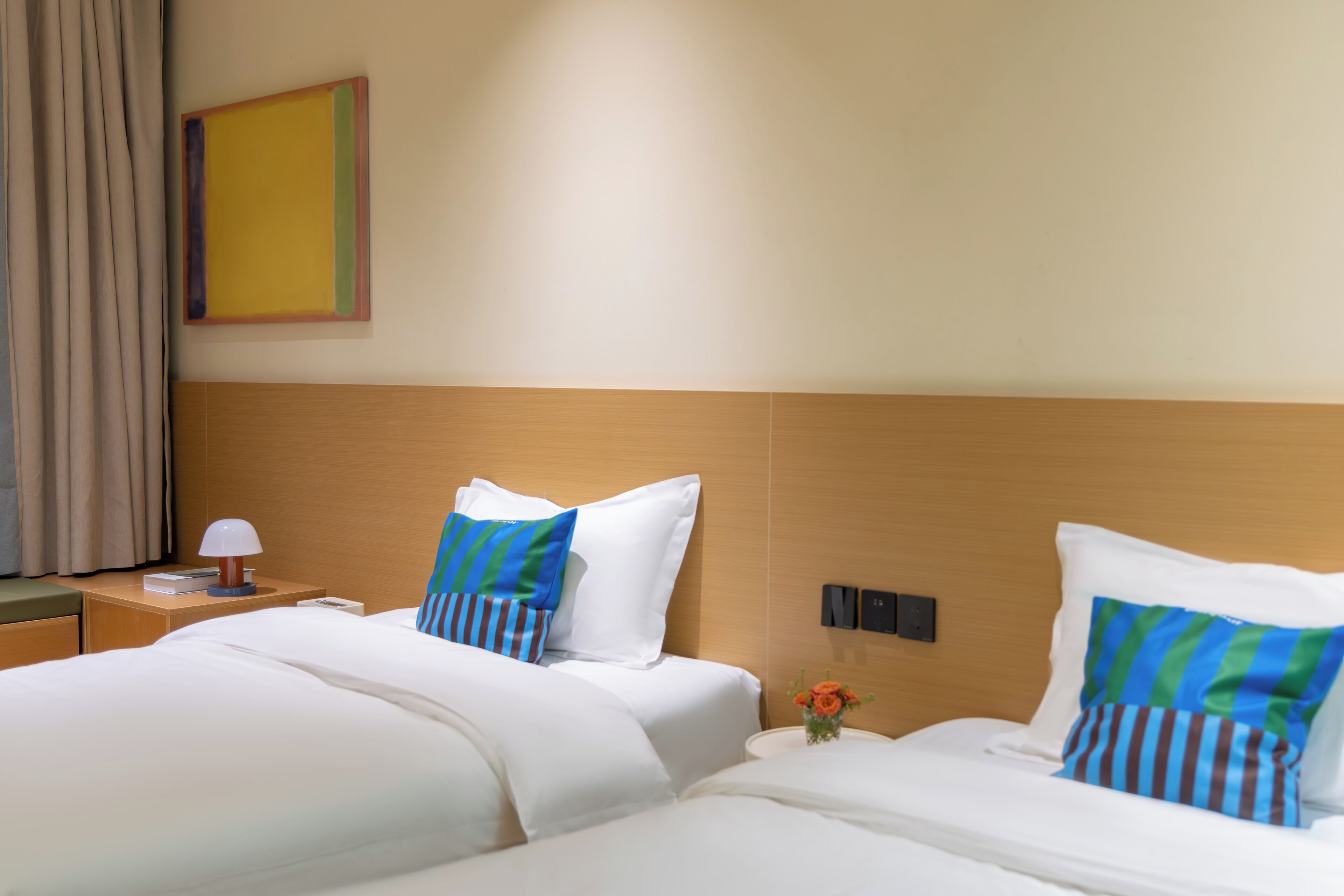 A hotel room with two beds, a nightstand, a lamp, a wall clock, and a framed picture.