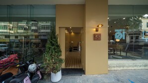 L'ingresso di un hotel con facciata in vetro, una pianta in vaso e uno scooter parcheggiato.