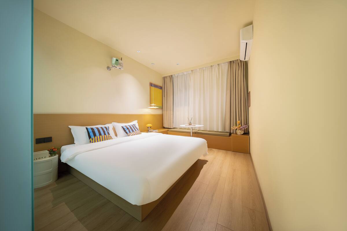 Une chambre d’hôtel avec un grand lit, des tables de chevet, une petite table avec une lampe et une fenêtre avec des rideaux.