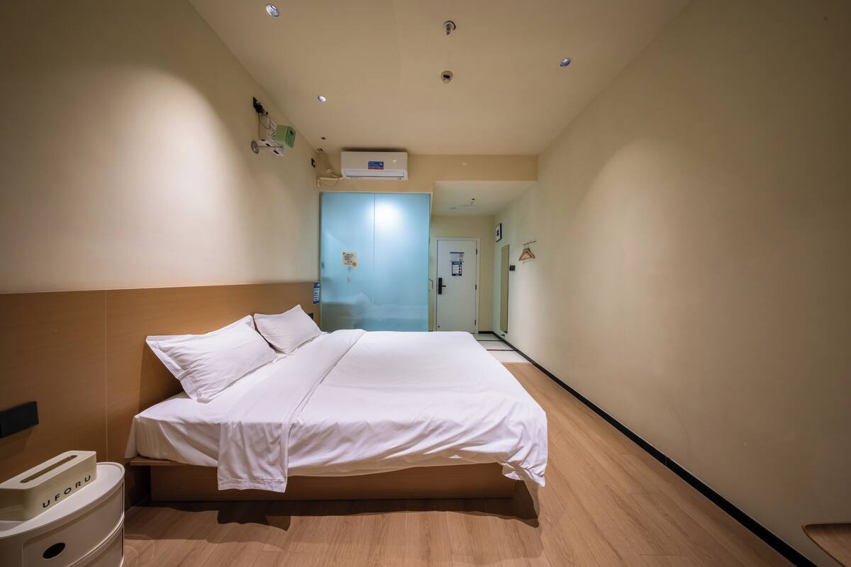 Une chambre d’hôtel comprenant un lit, une table de chevet, une poubelle et une porte donnant sur une autre pièce.