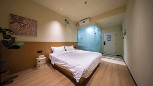 Una camera d'albergo con un letto, un comodino, un condizionatore d'aria a parete e una porta che dà su un'altra stanza.