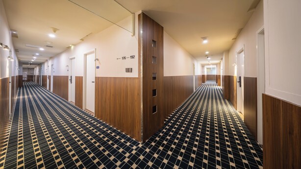 Pasillo de hotel con piso de diseño a cuadros, paneles de madera y puertas numeradas del 176 al 192.