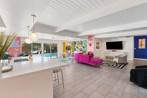 A modern living room with a pool view, a pink sofa, and a TV. - The Beverly - Pool, spa, firepits, putting green! (Palm Springs)
