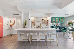A modern kitchen with a central island, bar stools, pendant lighting, and green cabinets. - The Beverly - Pool, spa, firepits, putting green! (Palm Springs)