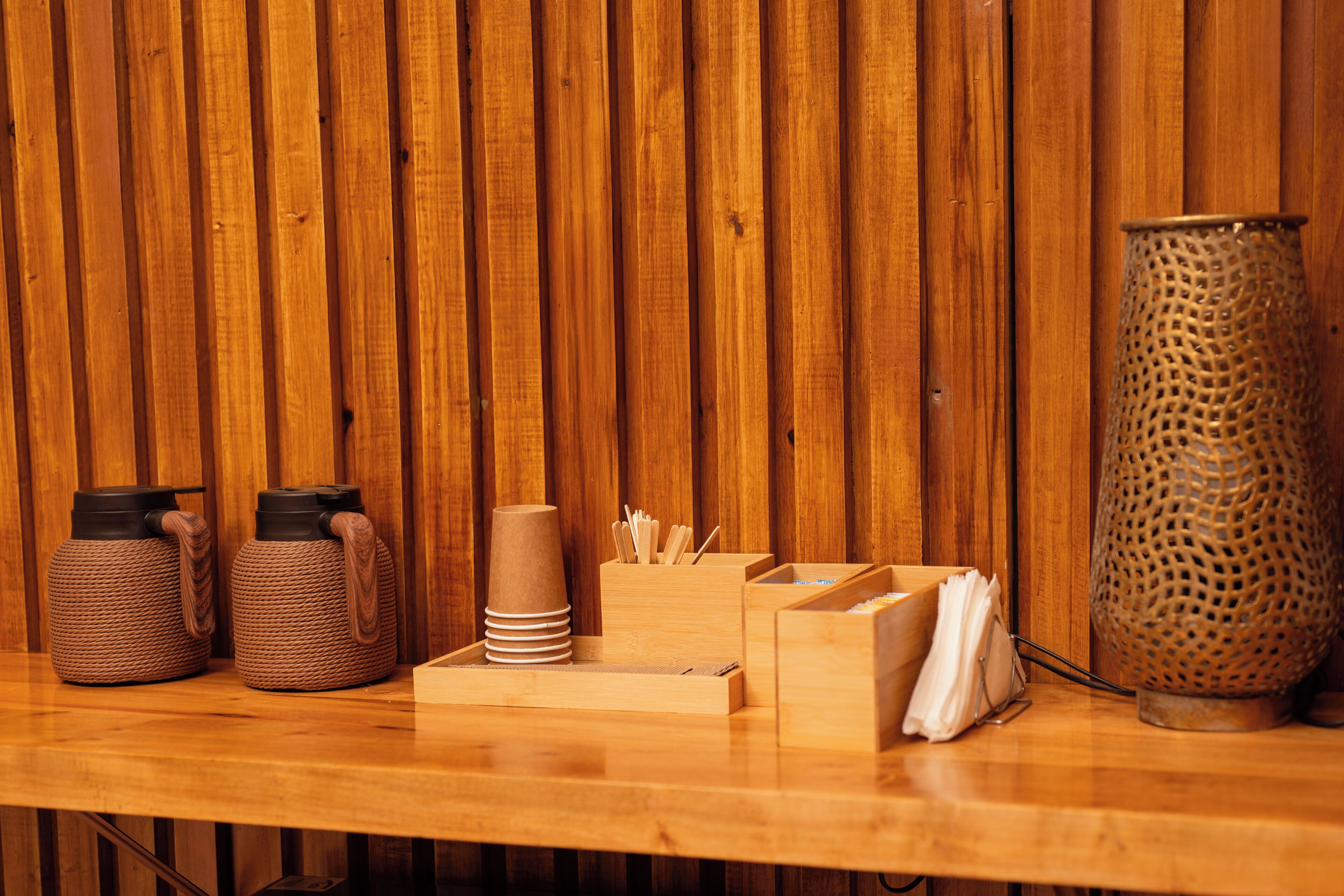 Un tavolo di legno con due contenitori intrecciati, una pila di tovaglioli, un vassoio con posate e un vaso in metallo forato.
