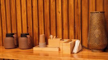 Un tavolo di legno con due contenitori intrecciati, una pila di tovaglioli, un vassoio con posate e un vaso in metallo forato.