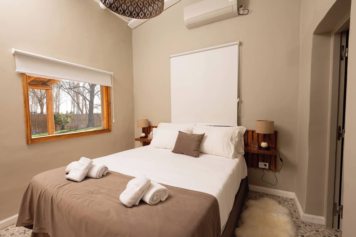 A bedroom with a large bed, two bedside tables with lamps, a window with a view, and a door.