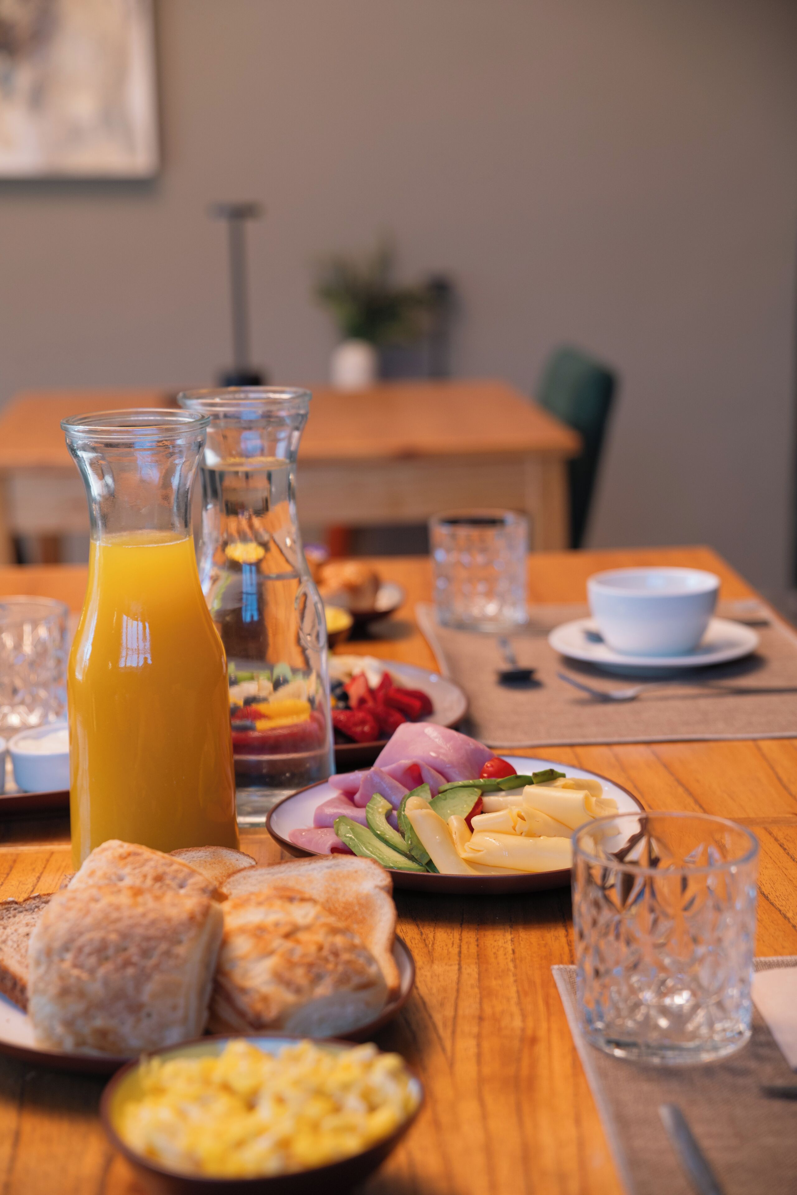 A breakfast table with various food items, a glass of orange juice, and a pitcher.