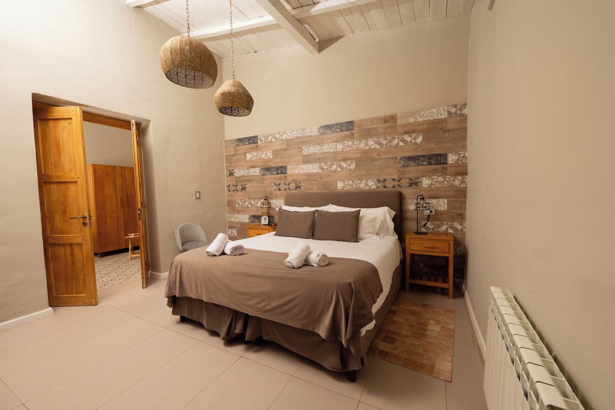 A bedroom with a bed, a chair, a nightstand, and a hanging light fixture.