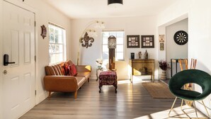A spacious living room with a sofa, a coffee table, and a green chair. There is a fireplace with a clock above it, and a wall with framed pictures. - Modern & Homely Entire House Orlando. Key Location! (Orlando)