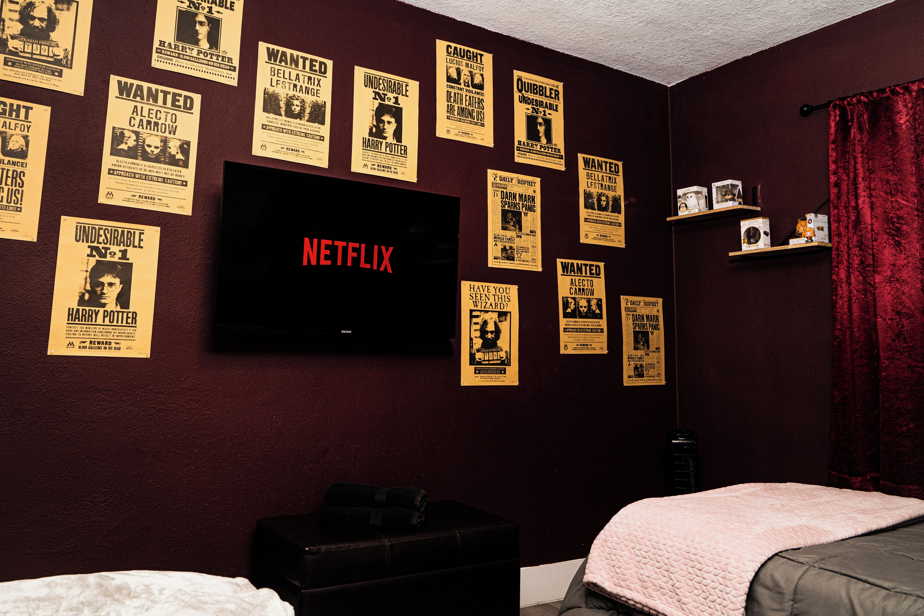 A room with a TV mounted on the wall displaying the Netflix logo, surrounded by various posters.