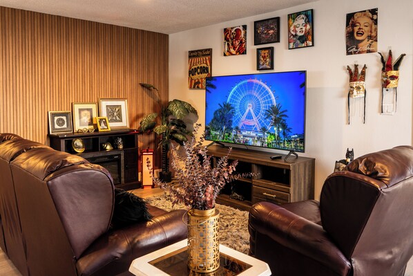 A living room with a TV displaying a Ferris wheel, leather sofas, framed pictures, and a decorative plant.