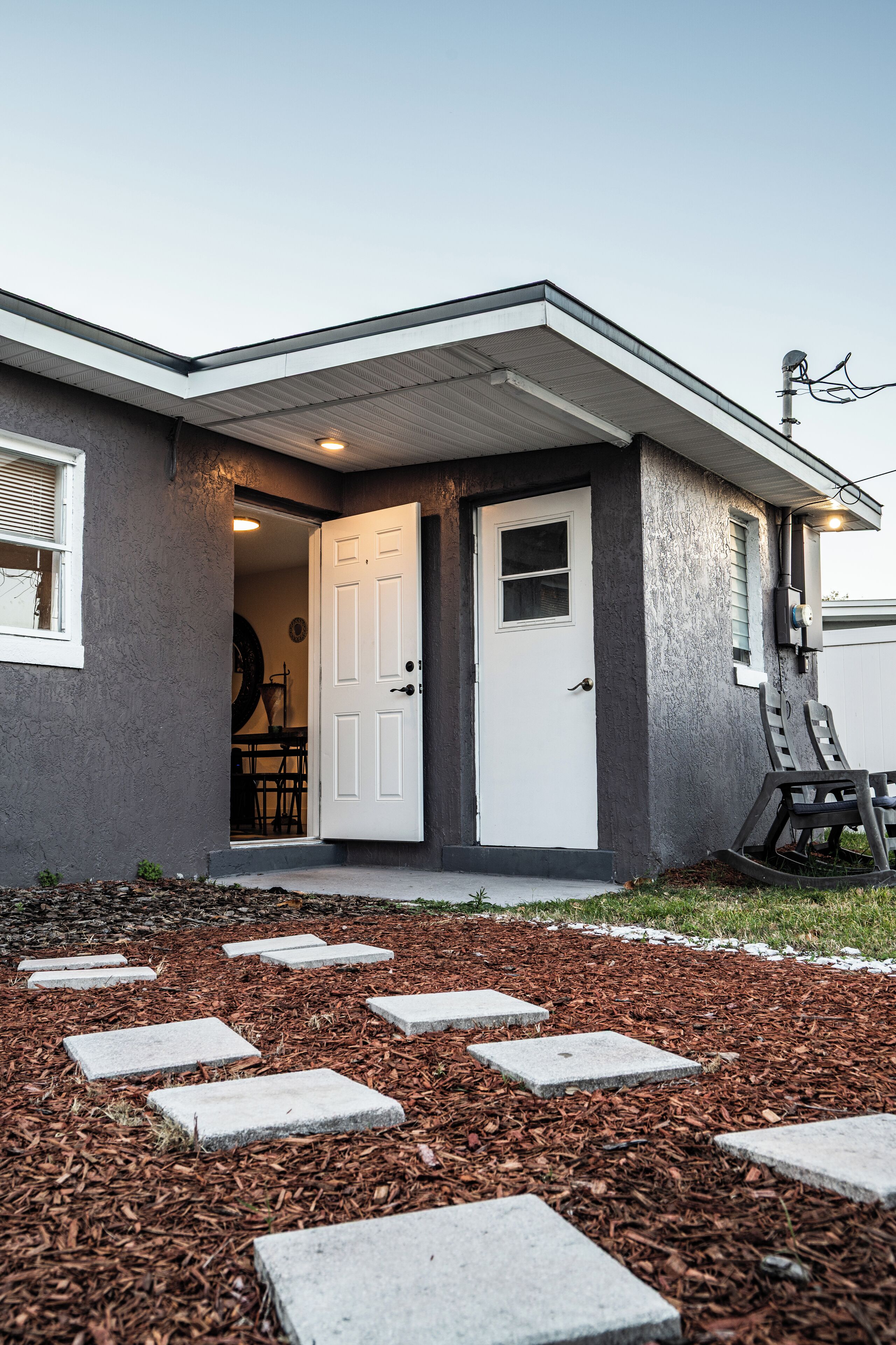 Une maison avec une porte blanche, un petit porche avec des pas de pierre et une porte de garage.