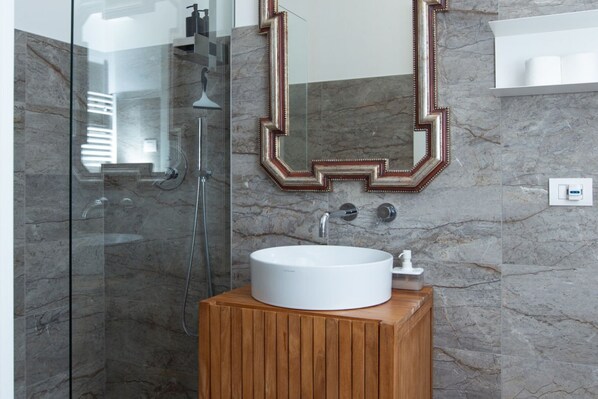 Une salle de bain moderne dotée d’une douche à parois de verre, d’un meuble-lavabo en bois avec un vasque blanche et d’un miroir à cadre géométrique.