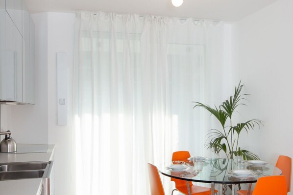 A modern kitchen with a stainless steel sink, a kettle, and a glass table set for dining.