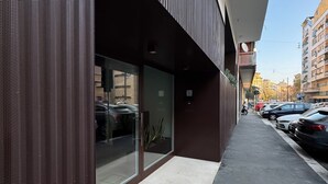 A modern building with a glass entrance, a parking area with cars, and a clear sky.