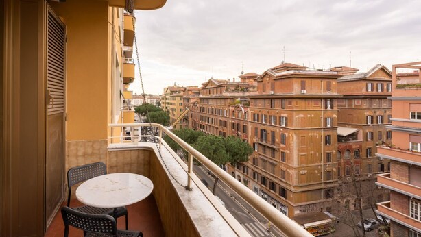 A balcony with a table and chairs, overlooking a street with historic buildings. - Ancient Roman Style - 7th Floor - Exclusive Apt (Roma)