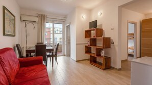 A modern living room with a red sofa, wooden shelves, a dining area with a table and chairs, and a TV on a wooden stand. - Ancient Roman Style - 7th Floor - Exclusive Apt (Roma)