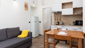 A compact living space with a kitchenette, a dining area, and a sofa with a yellow throw blanket. - Da Vinci - Exclusive Apartment - Navigli (Milano)