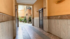 A corridor with tiled flooring, a black door, and a view of a courtyard with potted plants. - Da Vinci - Exclusive Apartment - Navigli (Milano)