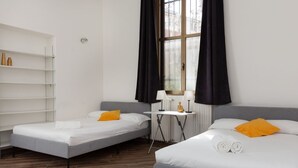 A hotel room with two single beds, a small table with a lamp, a radiator, and a window with black curtains. - Da Vinci - Exclusive Apartment - Navigli (Milano)