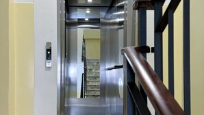 An elevator interior with a control panel, a wooden handrail, and a marble staircase in the background. - Humanitas - Exclusive Apartment (Rozzano)