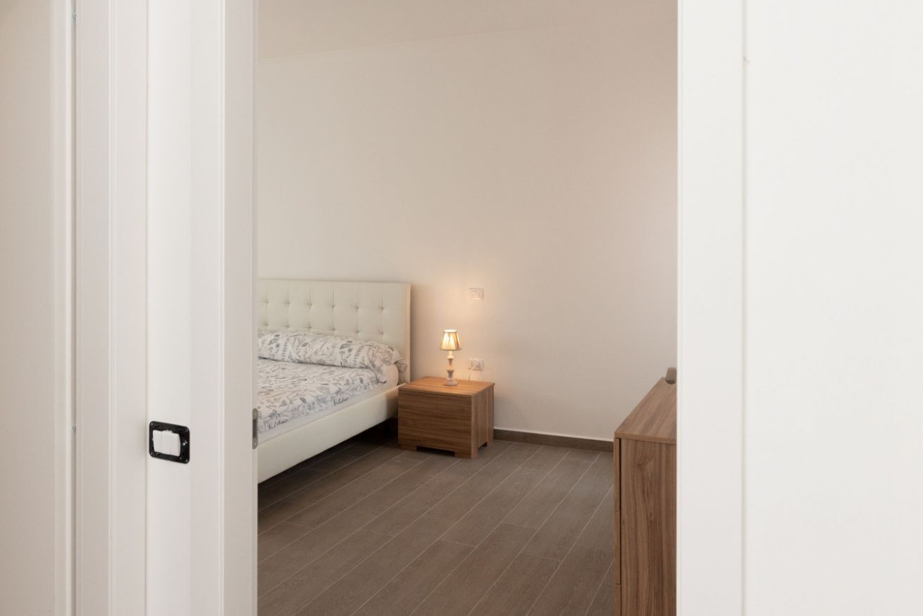 A bedroom with a bed, a bedside table with a lamp, and a wooden nightstand.