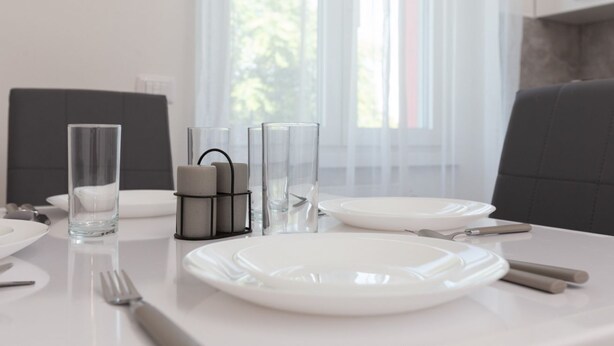 A dining table set with white plates, cutlery, and clear glassware, with a window in the background. - Humanitas - Exclusive Apartment (Rozzano)