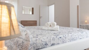 A bedroom with a bed, a bedside lamp, a mirror, and a door leading to another room. - Humanitas - Exclusive Apartment (Rozzano)