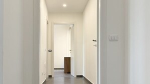 A narrow, well-lit hallway with white walls and a tiled floor, leading to a door at the end. - Humanitas - Exclusive Apartment (Rozzano)
