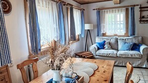 En hyggelig stue med et træbord, en sofa med blå puder og ternede gardiner.