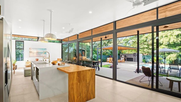 A modern kitchen with a central island, large windows, and a view of the outdoor patio area.