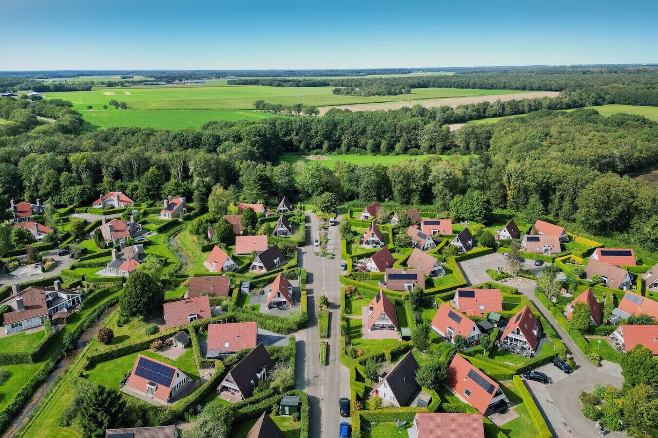 Een woonwijk met huizen in een rasterpatroon, omgeven door groene velden en bomen.