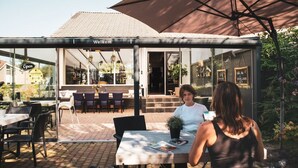 Un café al aire libre con un cartel de 'Welcome', mesas exteriores y vistas al interior.
