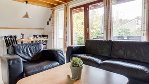 Un salón acogedor con techo de madera, sofás de cuero, una mesa de comedor con sillas y un ventanal con cortinas.