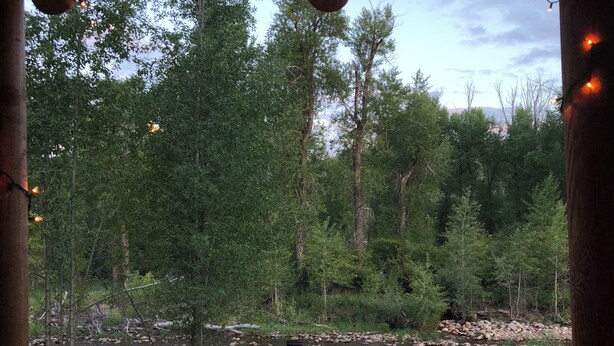 Un espace extérieur aménagé avec une table et des chaises, donnant sur une rivière et entouré d’arbres.