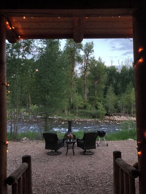 Un espacio al aire libre con mesa y sillas frente a un río, rodeado de árboles.
