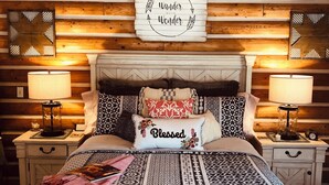 Une chambre confortable avec un plafond en bois, un lit recouvert d’une literie à motifs, deux tables de chevet avec des lampes et un panneau mural sur lequel on peut lire : « Explorez le monde avec émerveillement ».