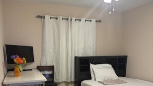 Un dormitorio con una cama, un escritorio con silla, un televisor y un ventilador de techo.
