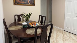 Un comedor con una mesa redonda, sillas, una planta en maceta y un cuadro en la pared.