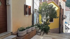 Une rue étroite avec un bâtiment jaune, des marches en pierre et des plantes en pot.