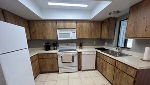 Una cocina compacta con armarios de madera, un refrigerador blanco, un microondas, un horno, un lavavajillas y un lavamanos.