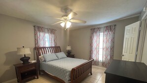 Un dormitorio con cama, mesitas de noche, ventilador de techo y cortinas.