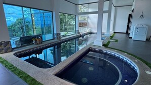 Una piscina interior moderna con paredes de vidrio transparente, borde de azulejos y una pequeña cascada.