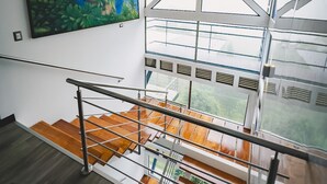 Un interior moderno con una escalera, un cuadro grande y ventanas amplias.
