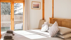 Une chambre à coucher avec un lit, des oreillers, un tableau encadré et une vue sur une terrasse en bois.