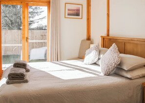 A bedroom with a bed, pillows, a framed picture, and a view of a wooden deck.