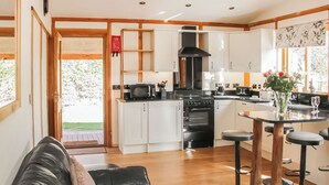 Une cuisine moderne avec des meubles blancs, une cuisinière noire et un coin repas comprenant une table en verre et des tabourets.